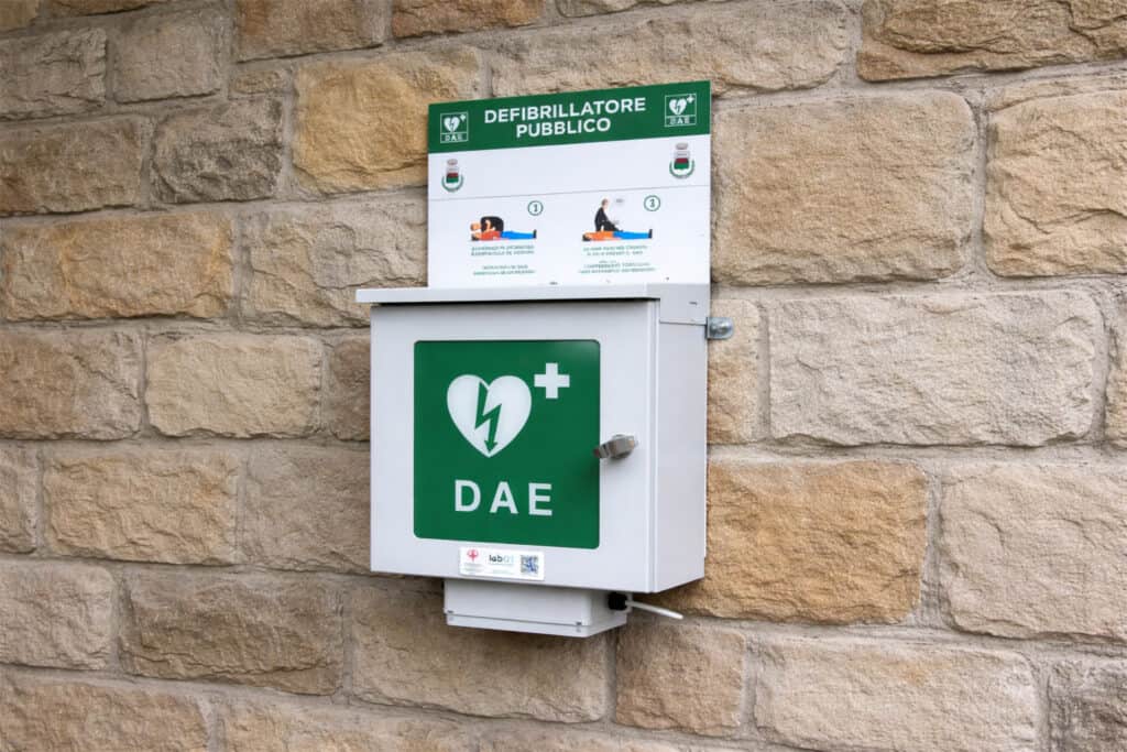 Defibrillatore pubblico con segnale DAE su parete in pietra.